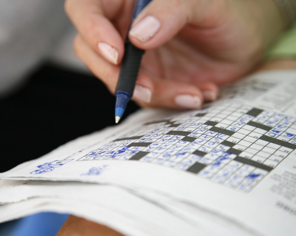 Hand solving a newspaper crossword puzzle.