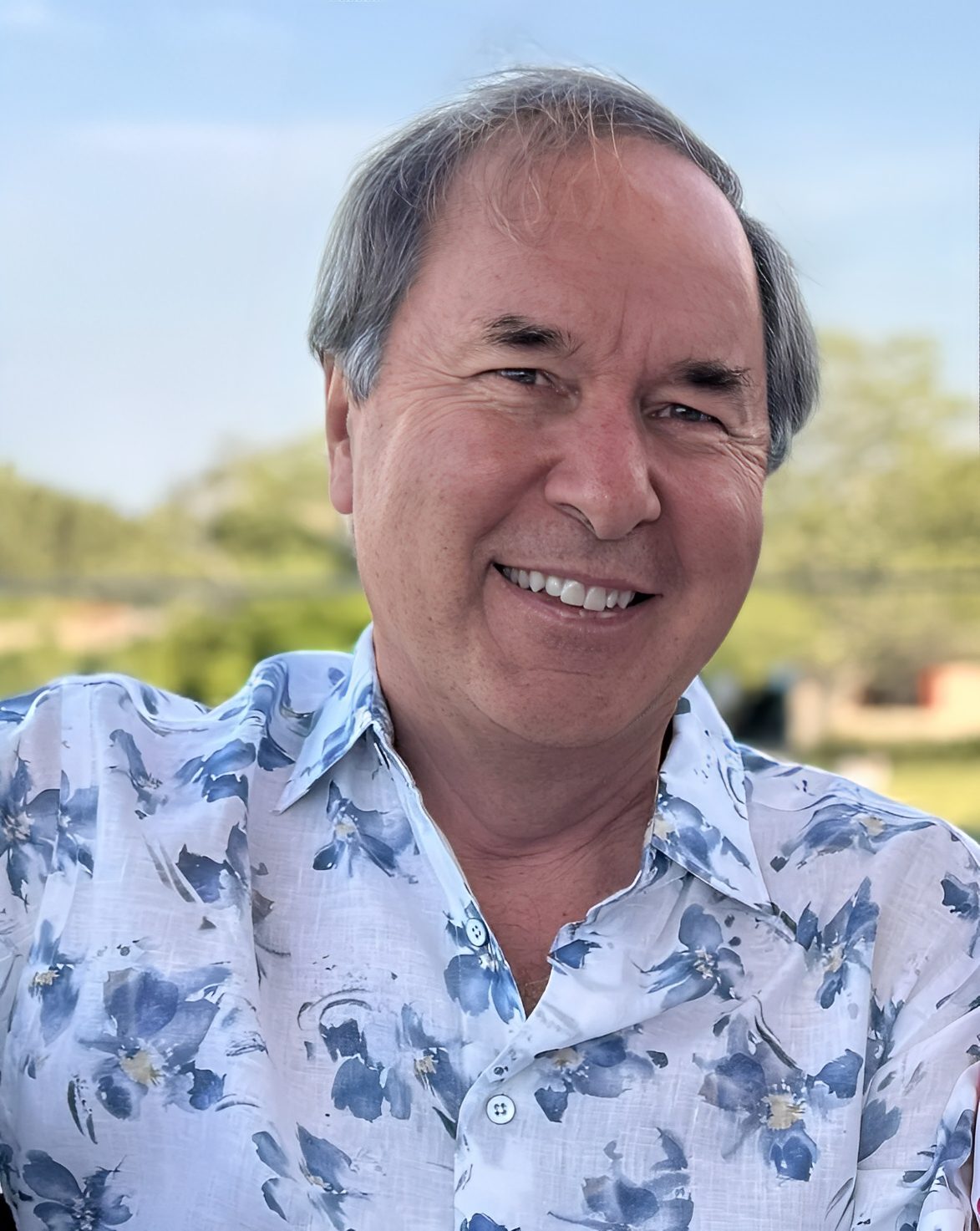 Smiling man in floral shirt outdoors.